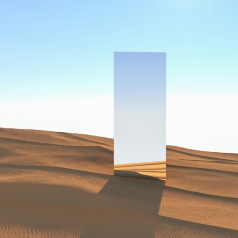 A rectangular mirror in the desert sand with a blue sky in the background.