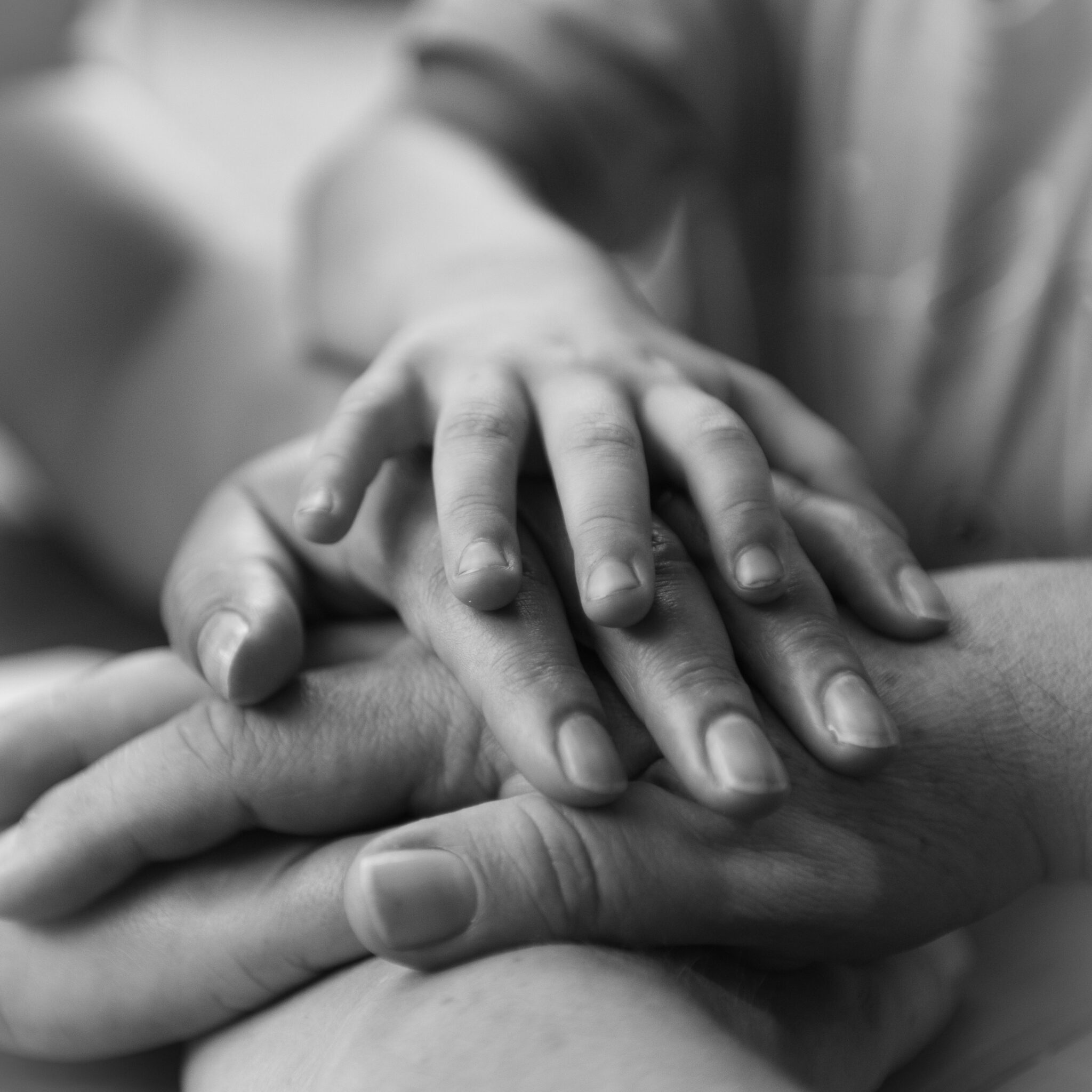 A black and white photo of peoples’ hands layered on top of each other.