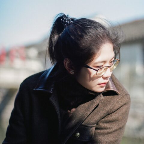 A woman wearing a brown coat and looking pensive.