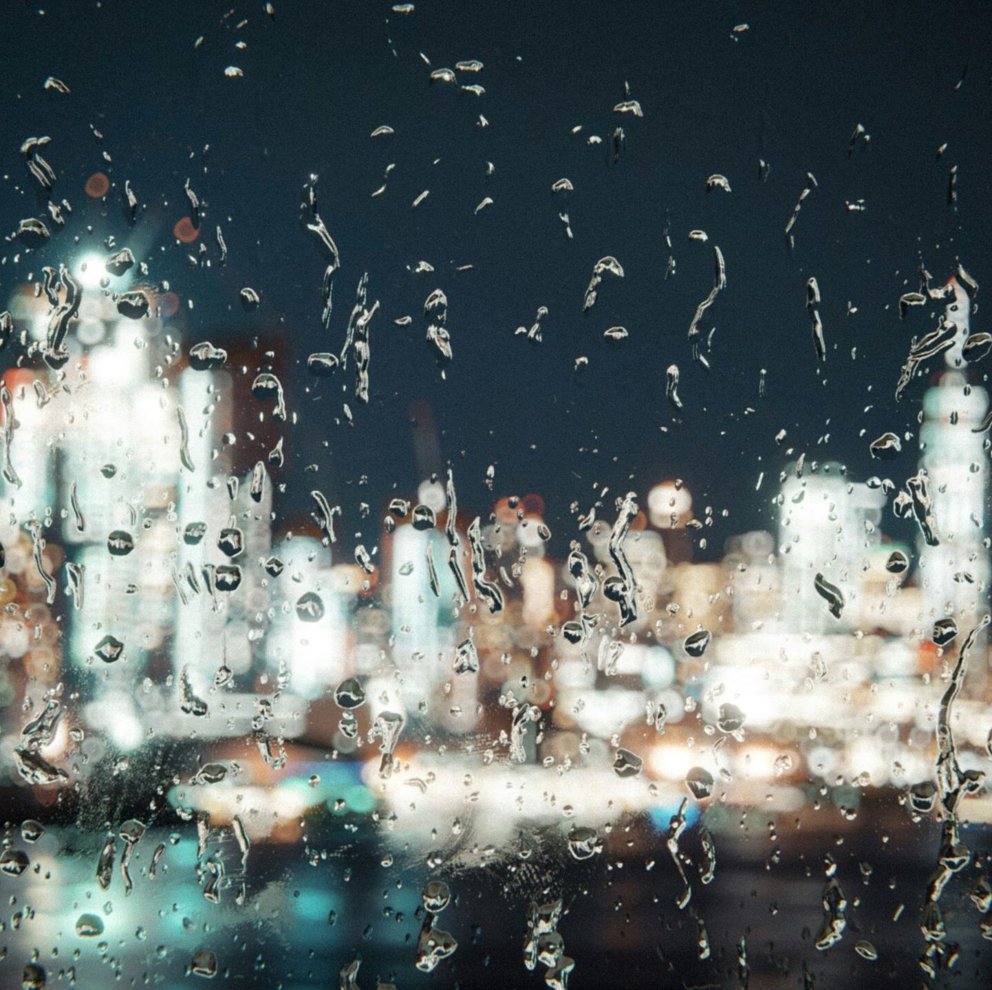 A blurred rainy night city scene seen through a window.